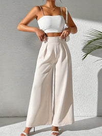 Frau in weißem Crop-Top und weiten cremefarbenen Hosen, Sommermode, eleganter Look.