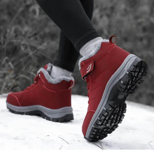 Rote Stiefel getragen im Schnee, ein Fuß angehoben, sodass das kräftige Sohlenprofil sichtbar ist 6