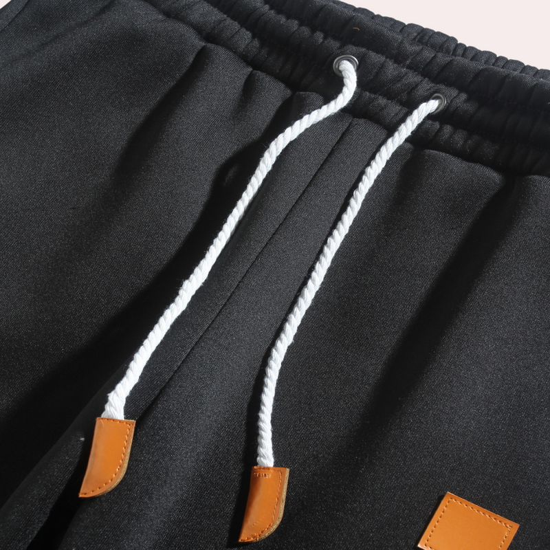 Schwarze Jogginghose mit weißen Kordeln und braunen Lederakzenten, sportlich, bequem.