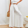 Frau in weißer, weiter Hose und Top, hält eine Bambustasche, Sommermode, eleganter Look.