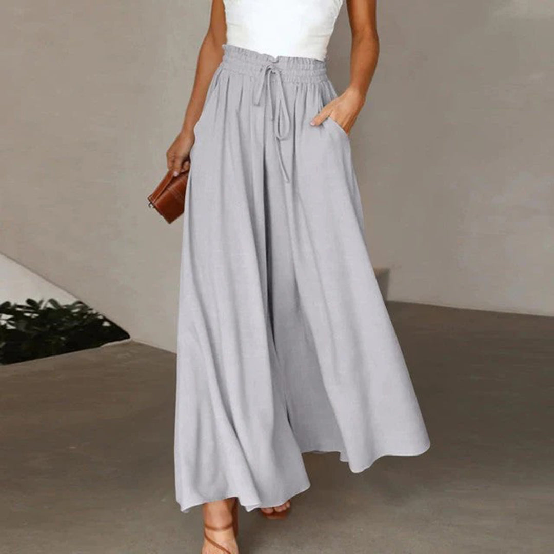 Frau in grauer, weiter Hose mit Kordelzug, weißem Top, brauner Tasche, eleganter Look.