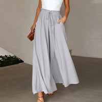 Frau in grauer, weiter Hose mit Kordelzug, weißem Top, brauner Tasche, eleganter Look.