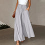 Frau in grauer, weiter Hose mit Kordelzug, weißem Top, brauner Tasche, eleganter Look.