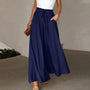 Frau in blauer, weiter Hose mit hoher Taille und weißem Top, hält braune Tasche.