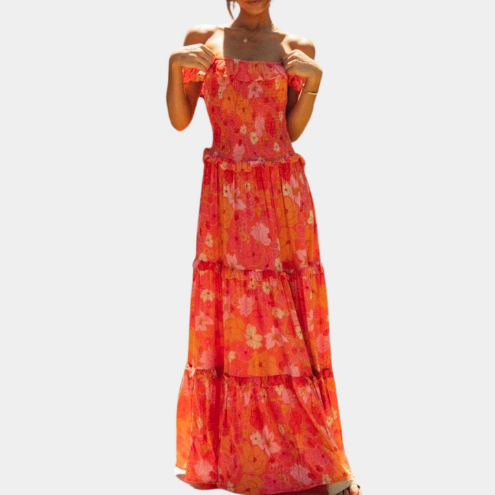 Frau in langem, schulterfreiem, geblümtem Sommerkleid in Rot- und Orangetönen.