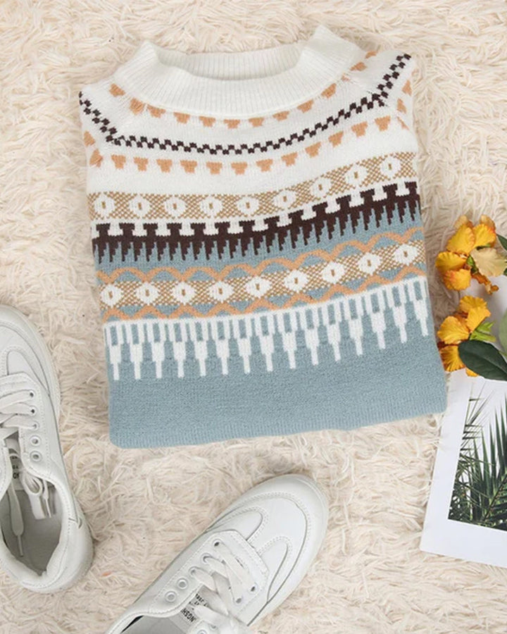 Gefalteter Strickpullover mit Norwegermuster in Weiß und Blau auf Teppich neben weißen Sneakers.