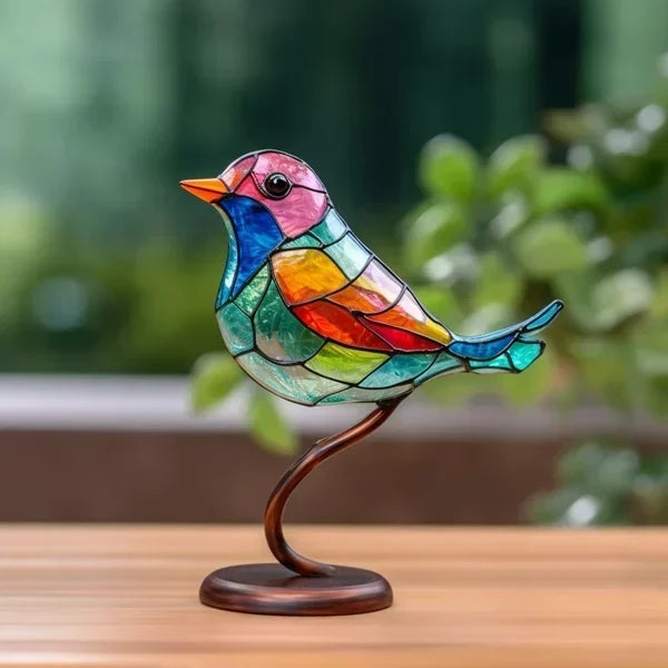 Einzelner bunter Glasmosaik-Vogel auf geschwungenem Metallstiel mit runder Holzbasis, vor grünem Pflanzenhintergrund auf 1