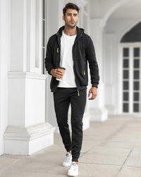 Model im schwarzen Anzug mit offener Jacke über weißem T-Shirt, geht mit Kaffeebecher durch einen Säulengang 24