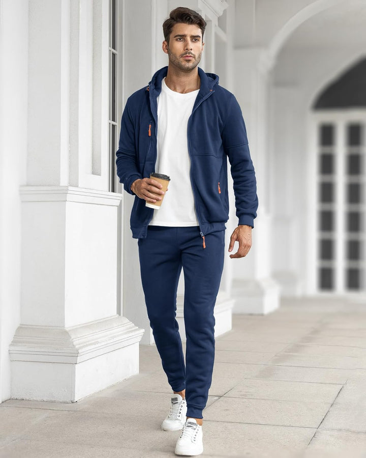 Mann im marineblauen Anzug mit offener Jacke über weißem Shirt, hält einen Kaffeebecher und läuft durch eine Säulenhalle 6