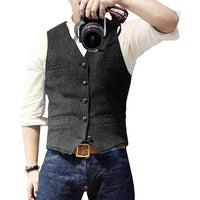 Mann mit grauem Wollweste, weißem Hemd, Jeans, hält Kamera.