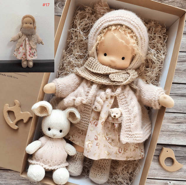 Puppe mit Wollhaube, Strickjacke und Blümchenkleid im Karton, daneben ein weißer Strickhase und Holzspielzeug 2