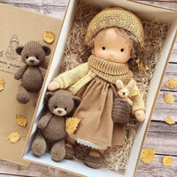 Puppe in Senfgelb und Braun mit Strickmütze und Schal im Karton, begleitet von zwei Strickbären 5