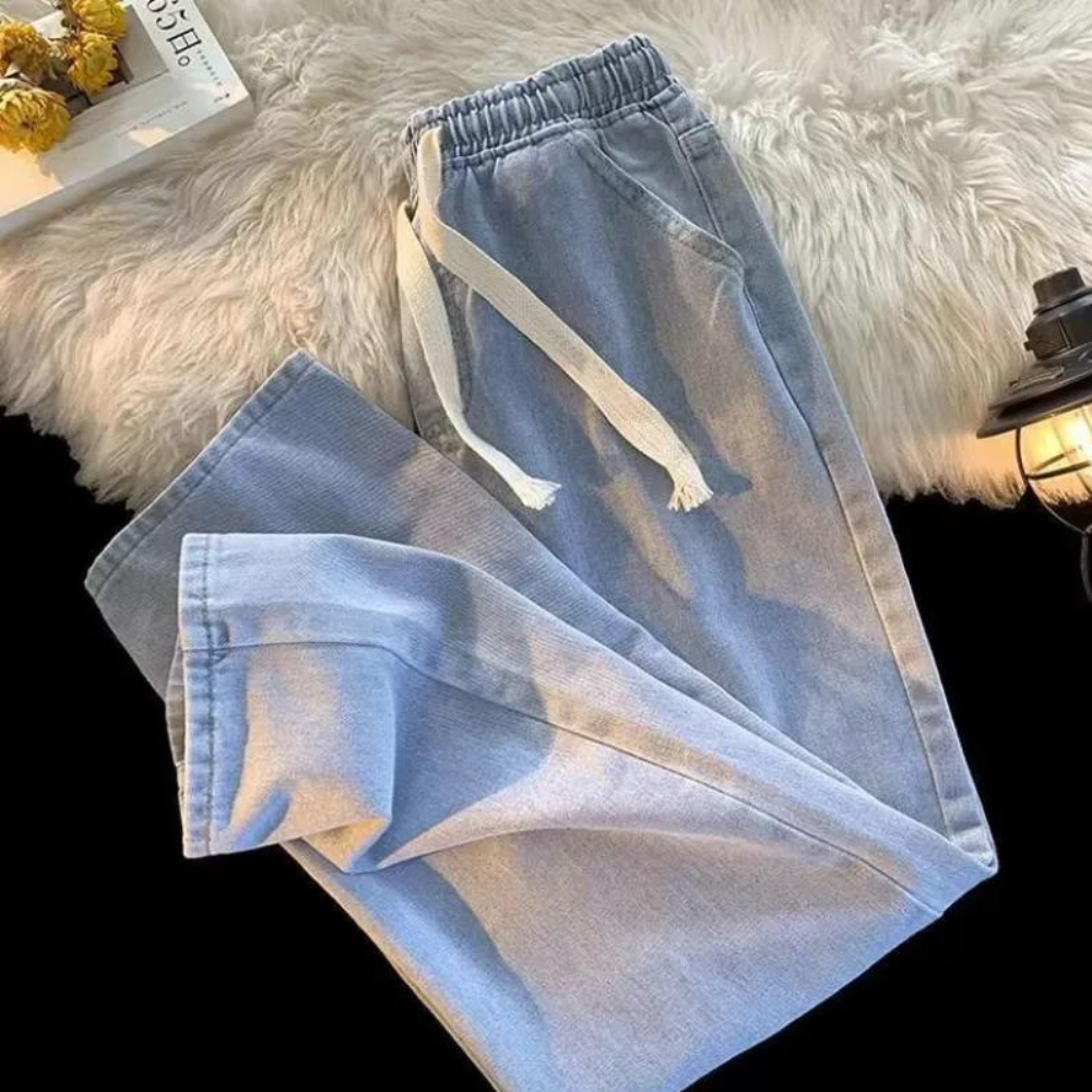 Hellblaue Jogginghose aus Denim mit Kordelzug auf weißem Fellteppich, gemütliche Freizeitmode.