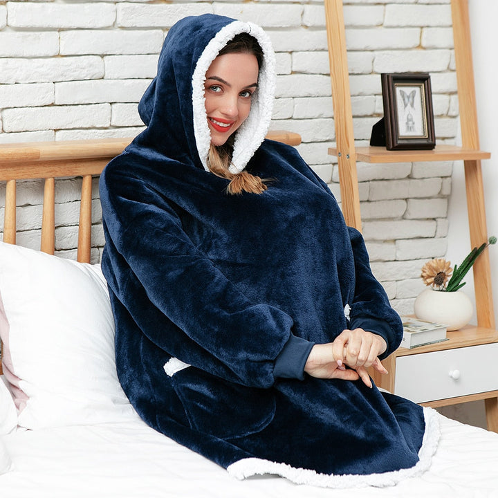 Frau in dunkelblauem, flauschigem Hoodie-Decke auf Bett, gemütliche Winterkleidung.