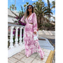Frau in lila Maxikleid mit Blumenmuster, Sonnenbrille, Palme im Hintergrund, Sommermode.