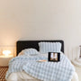 Bett mit hellblauer Noppen-Plüschdecke und passenden Kissen, darauf Laptop und Kerzenschale, Lampe links 5