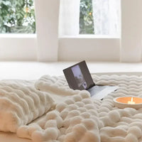 Cremeweiße Plüschdecke mit Wellenstruktur im Vordergrund, dahinter Laptop und Kerzenschale vor einem Fenster 7